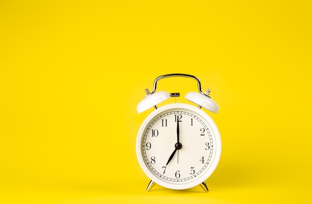 White alarm clock on a yellow background isolated closeup