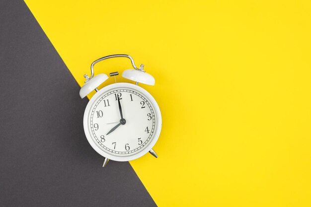 White alarm clock on a yellow and green background flat lay