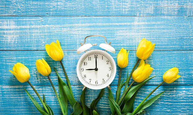 White alarm clock and yellow tulips on a blue background top view