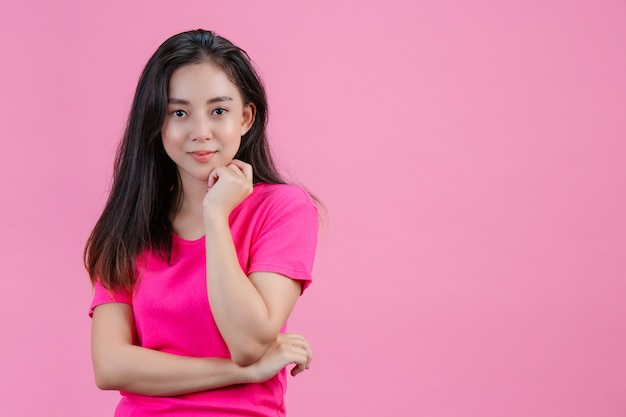 A white Asian woman puts her left hand against her chin on a pink .