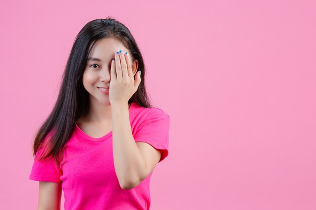 백인 아시아 여자는 그녀의 왼손을 분홍색의 한쪽 눈에 넣습니다.