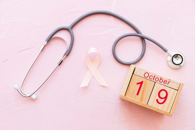 White awareness ribbon with 19th October wooden box and stethoscope on pink backdrop