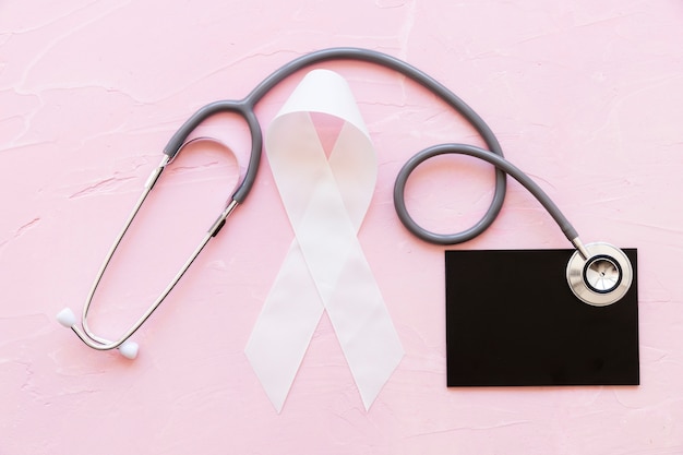 White awareness ribbons with stethoscope over slate on pink background