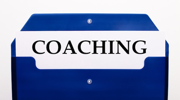 On a white background, a blue folder for papers. in the folder is a sheet of paper with the word coaching
