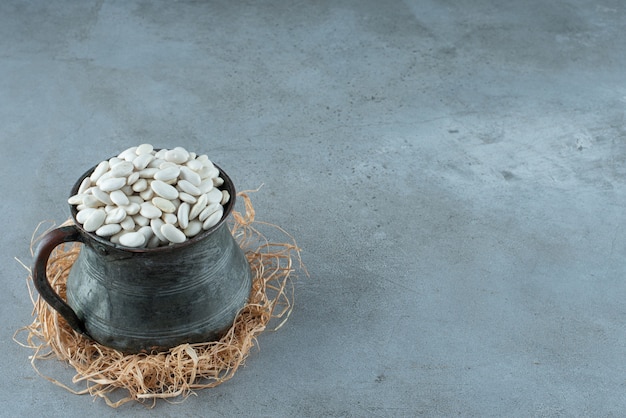 乾いた草の上の金属製のエスニックポットの白インゲン豆。高品質の写真