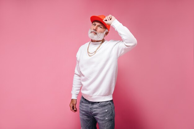 White bearded man in orange cap posing on pink wall