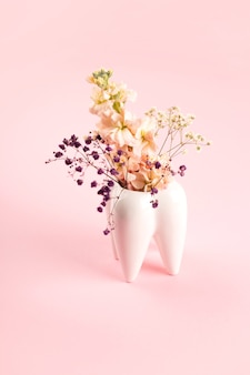 Белая большая зубная ваза с цветами на розовом фоне работы и эстетики стоматолога-ортодонта