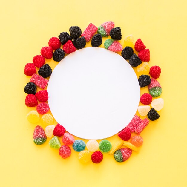 White blank frame surrounded with colorful jelly candies on yellow background