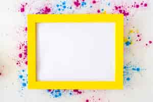 Free photo white blank frame with yellow border on holi color powder over white background