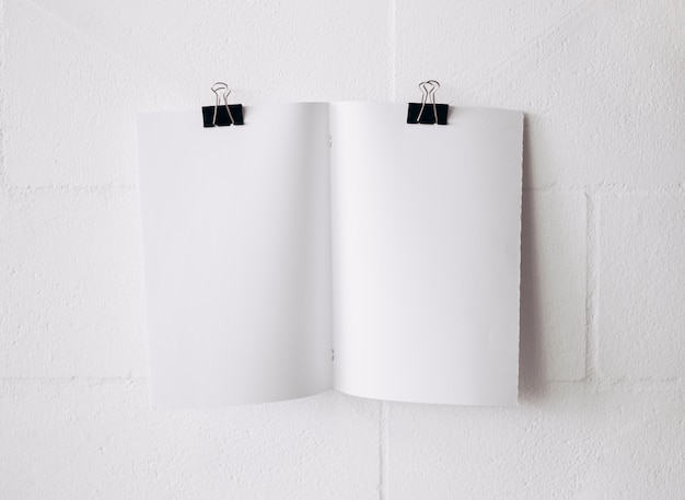 無料写真 白い空白の紙は白い壁を背景にした白い紙の上のブルドッグペーパークリップで添付します。