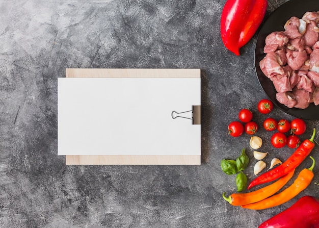 White blank paper on clipboard with ingredients for making meat on textured backdrop