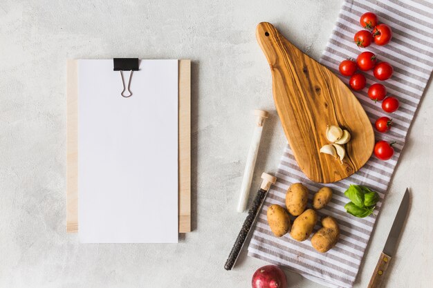 White blank paper on clipboard with vegetables and spices on white texture background