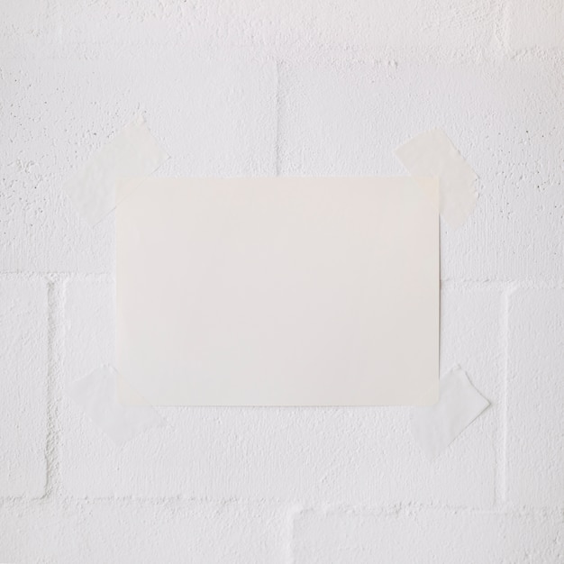 White blank paper stick with tape on white wall backdrop