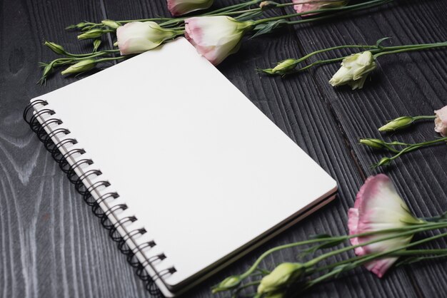 White blank spiral notepad with purple eustoma flowers over the wooden desk