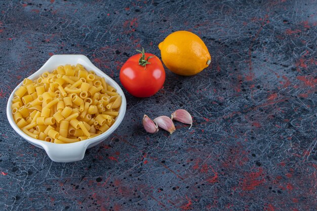 A white board of raw pasta with fresh red tomatoes and lemon on a dark background .