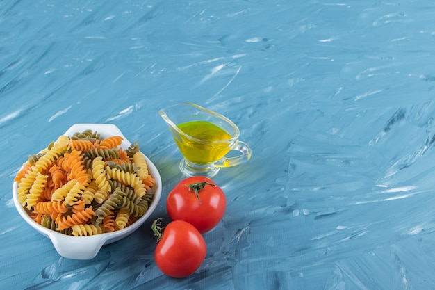 A white board of raw pasta with oil and fresh red tomatoes on a blue background. 