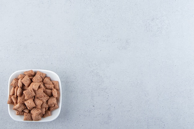 White bowl of chocolate pads cornflakes on stone surface