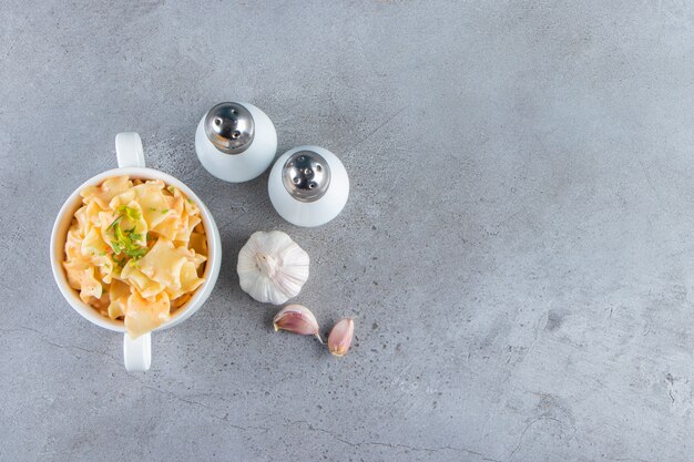 White bowl of delicious macaroni with garlic and salt on stone background. 