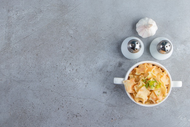 White bowl of delicious macaroni with garlic and salt on stone background. 