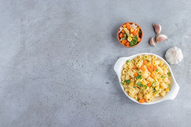 White bowl of delicious pasta with fresh salad on stone background. 