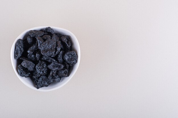 White bowl of dried plum fruits placed on white background. High quality photo