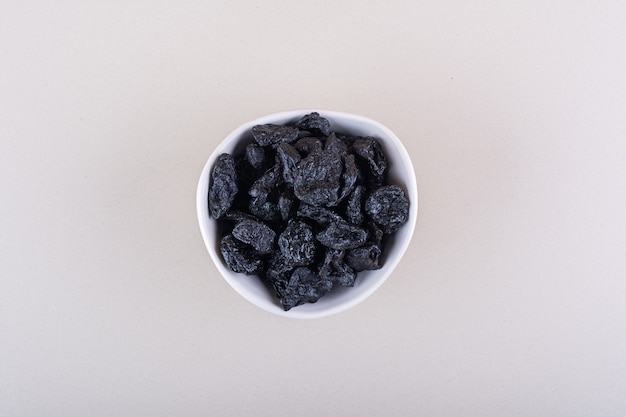 White bowl of dried plum fruits placed on white surface. High quality photo