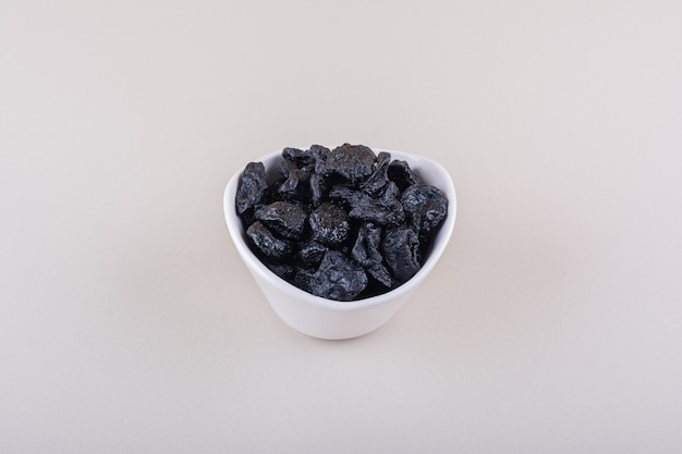 White bowl of dried plum fruits placed on white surface. High quality photo