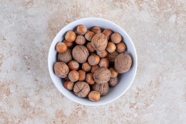 A white bowl full of healthy macadamia nuts and walnuts placed on a stone surface.