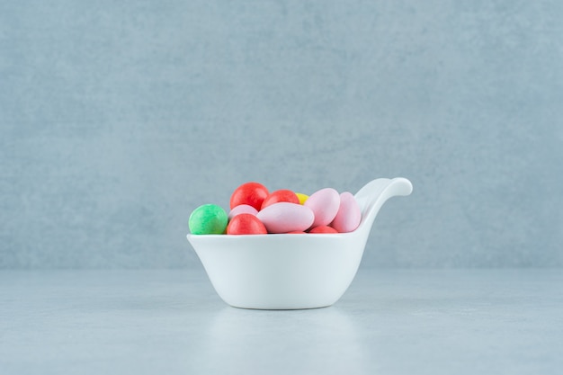 A white bowl full of round sweet colorful candies on white background . High quality photo