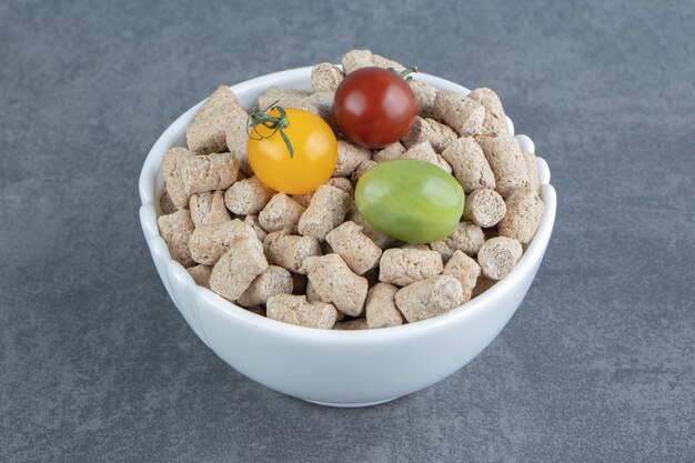 A white bowl full of rye crispy cereals and colorful tomatoes .