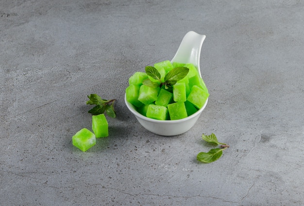 Foto gratuita una ciotola bianca piena di dolci caramelle verdi con foglie di menta su una pietra.