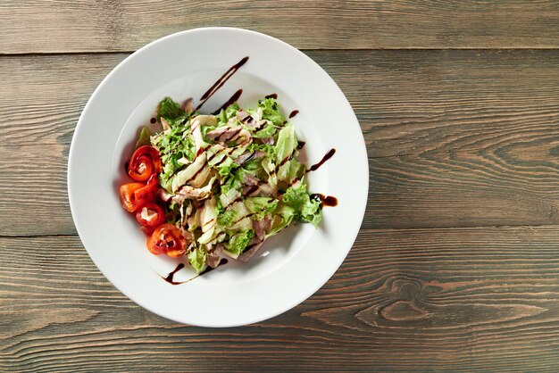 A white bowl full of vegetable salad with grilled chicken,paprika,lettuce leaves and sauce. Looks delicios and tasty.