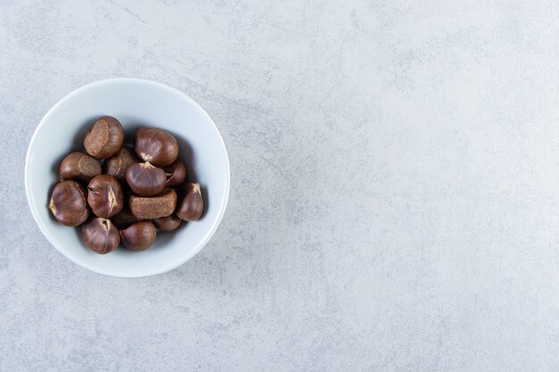 White bowl of many crunchy chestnuts on stone background.