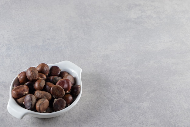 White bowl of organic shelled chestnuts on stone background. 