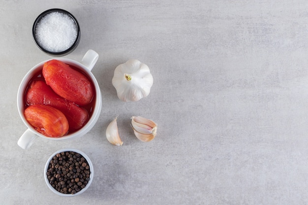 White bowl of pickled tomatoes placed on stone background.