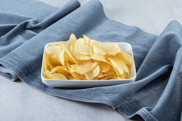 Free photo white bowl of salted potato chips on stone.