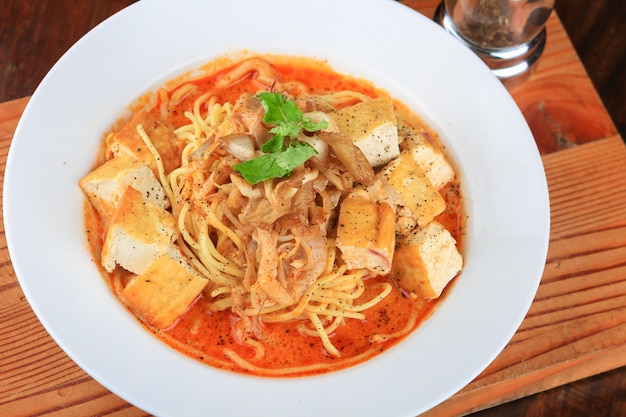 White bowl of soup with some spaghetti and bread pieces decorated with greens