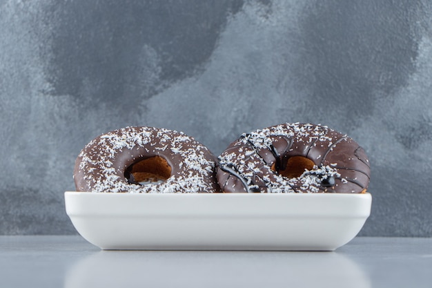 White bowl of two chocolate donuts on stone background. High quality photo