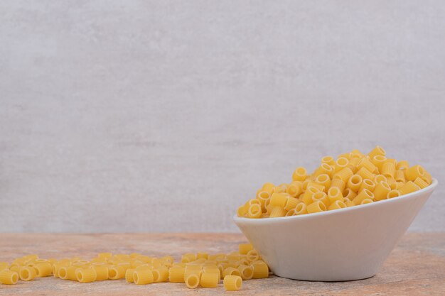 A white bowl of unprepared macaroni on marble background. High quality photo