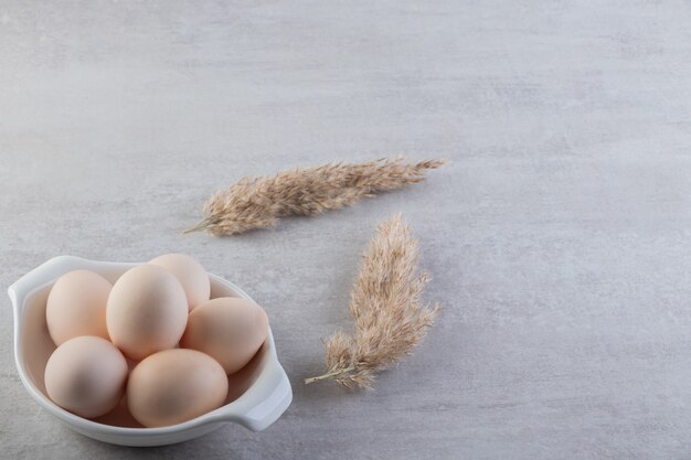 White bowl of white raw eggs on stone table.