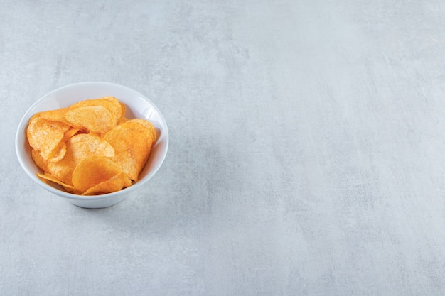 Free photo white bowl with delicious potato chips placed on stone.