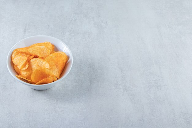 White bowl with delicious potato chips placed on stone.