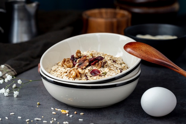 White bowl with musli and a wooden spoon with an egg on a grey background