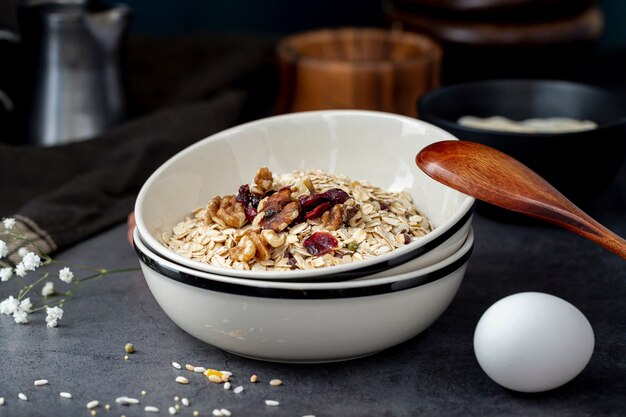 White bowl with musli and a wooden spoon with an egg on a grey background