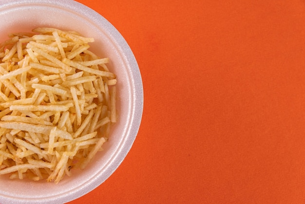 White bowl with potato straw on orange background