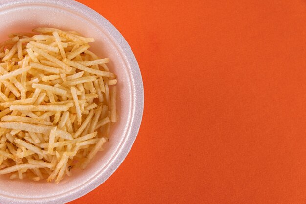 Белая миска с картофельной соломкой на оранжевом фоне