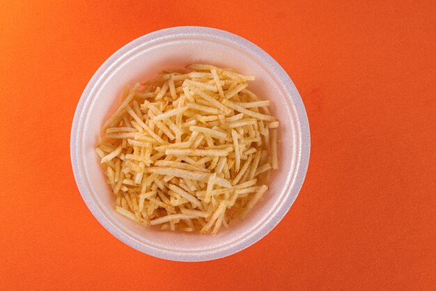 White bowl with potato straw on orange surface