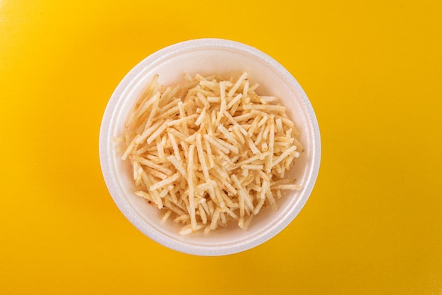 White bowl with potato straw on yellow background