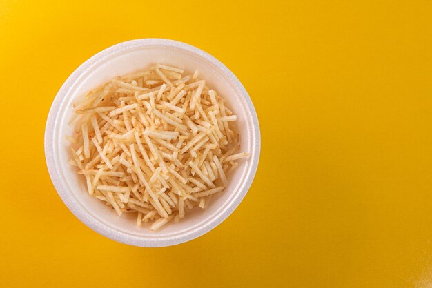 White bowl with potato straw on yellow background