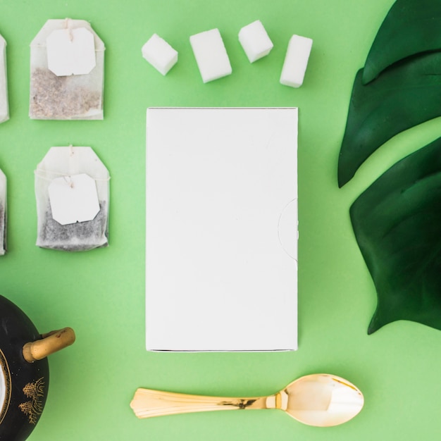 White box, sugar cubes and tea bag on green background